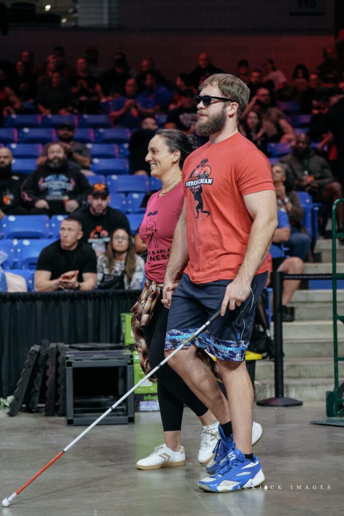 Evan is at a Strongman competition walking with a guide.