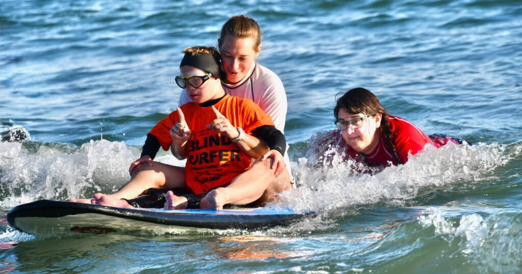 child surfing in the ocean with the help of a volunteer