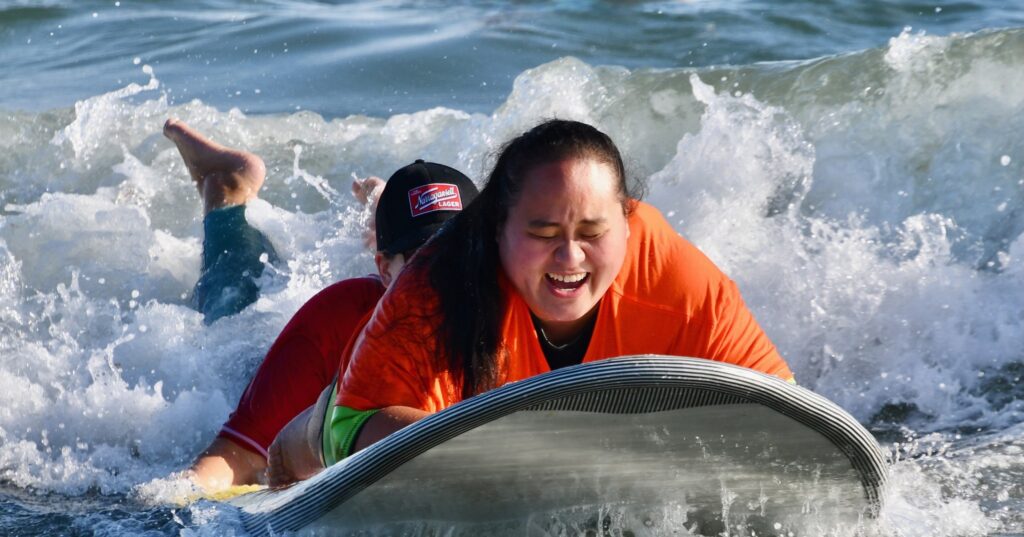 adult surfing in the ocean with the help of a volunteer