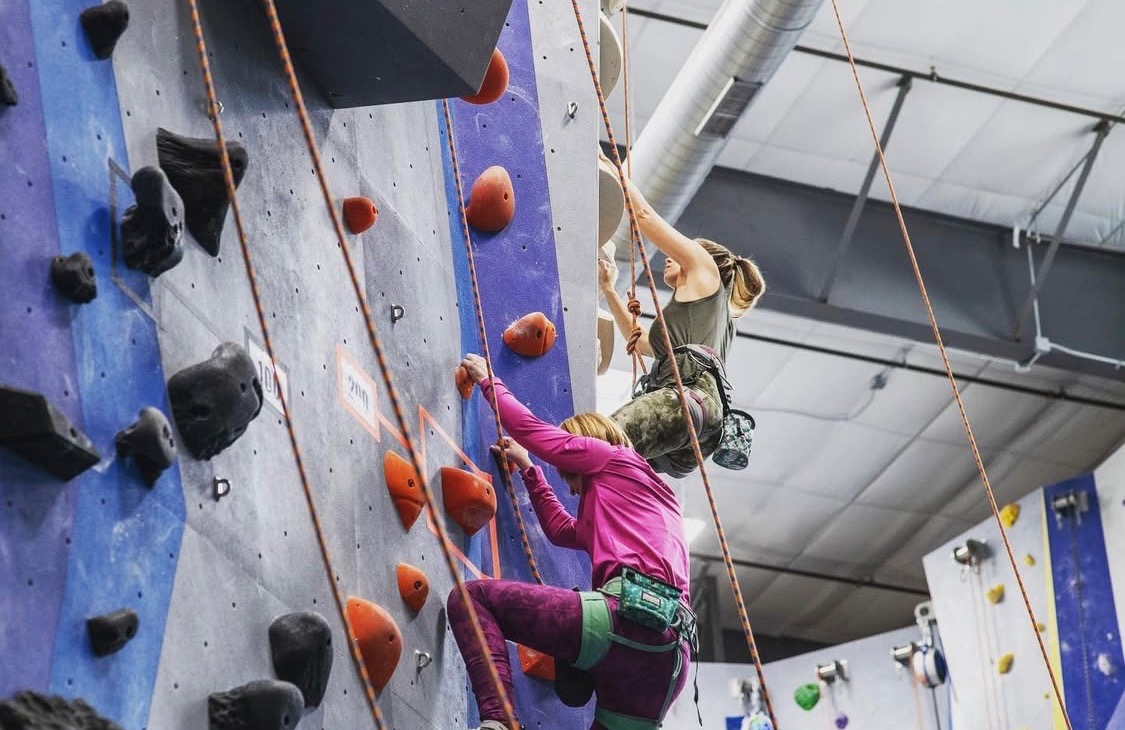 Kara and another climber are lead climbing in a rock climbing gym.