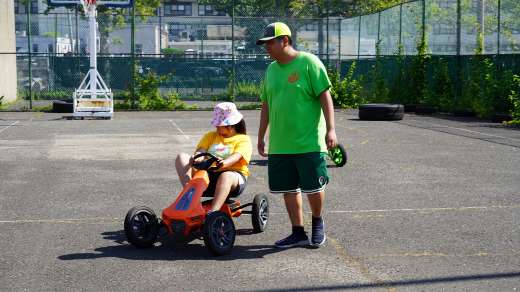 In this photo, a girl is driving a "go-kart" of sorts with the help of a guide.