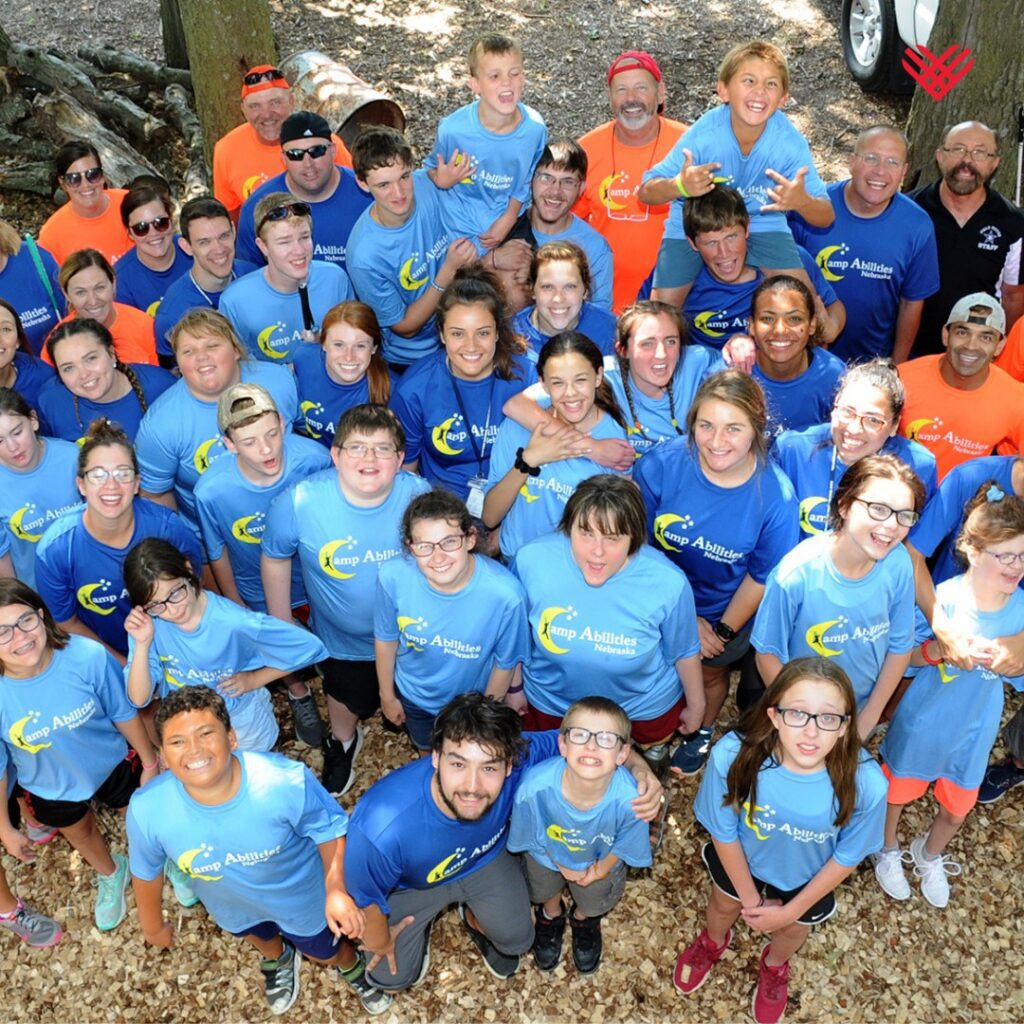 A group of children at Camp Abilities Nebraska are looking up at a camera smiling. 